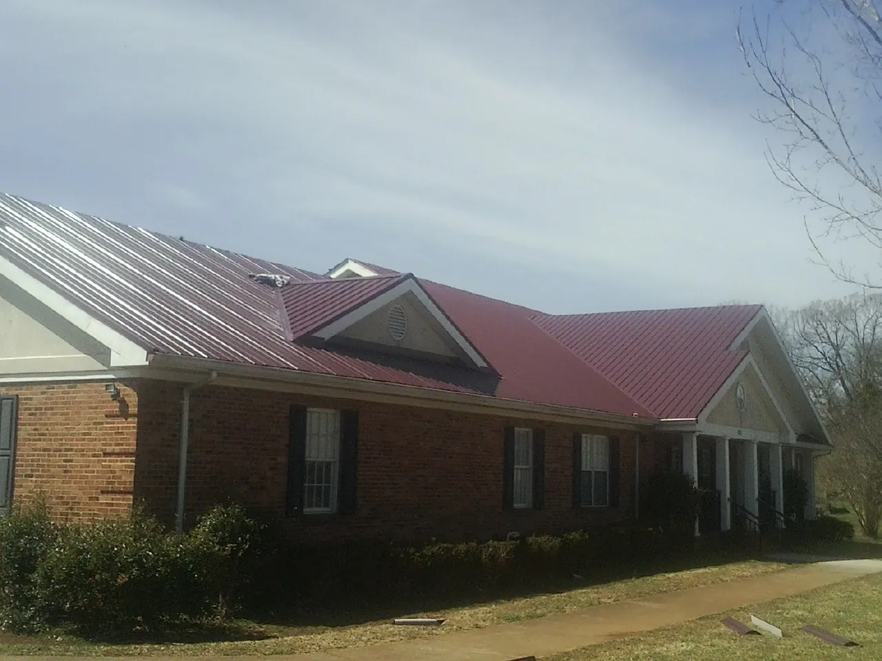 Red metal roof with gabled entries on a long brick building, from a Hail Damage Roof Repair job in Gilbertsville