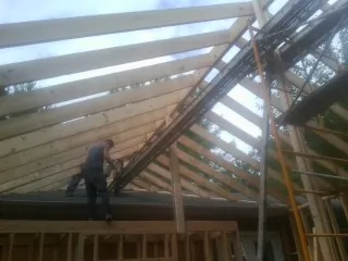 Rafters going up over a new addition with a worker on the wall in Gilbertsville