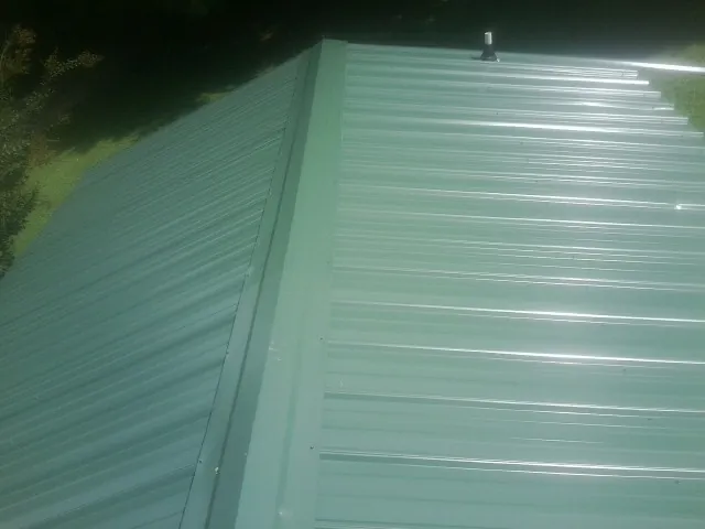 New green metal panels meeting at the ridge of a roof — Flat Roof Repair work by our crew in Gilbertsville