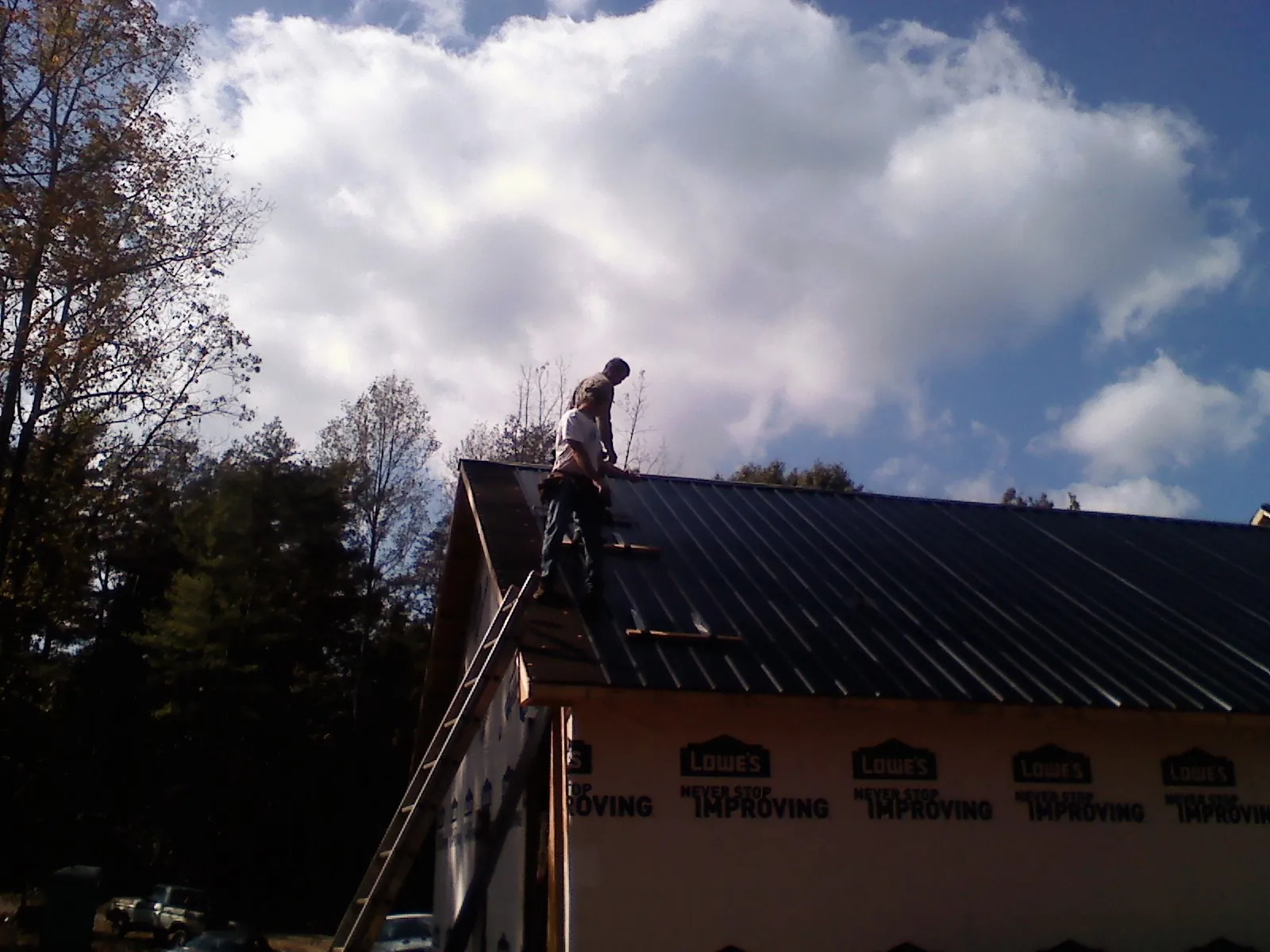Roofer fastening dark metal panels high against a cloudy sky, from a Roof Inspection job in Gilbertsville