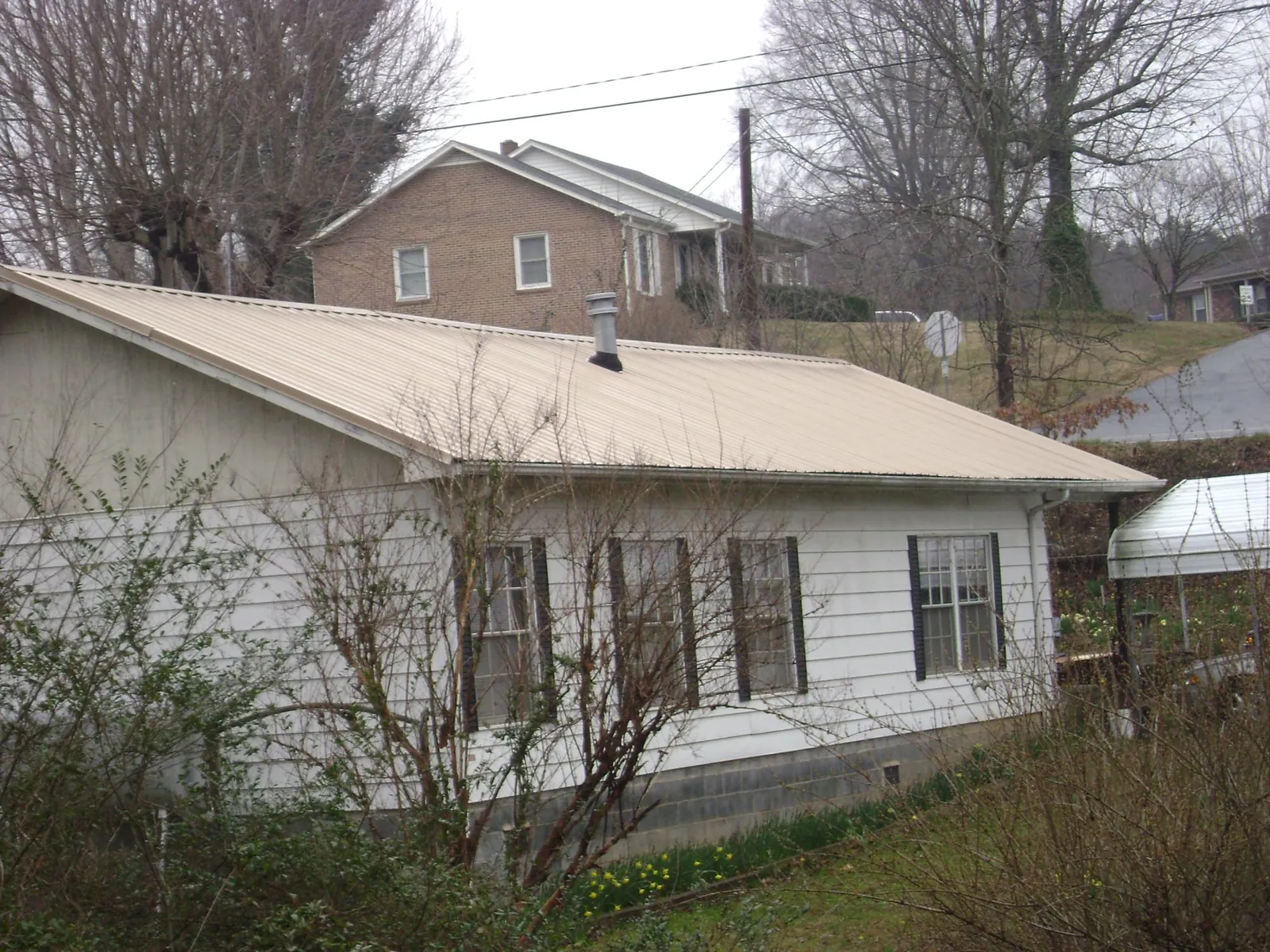 Tan metal roof on a white sided house set into a hillside — Commercial Roofing by Roofing Brothers in Gilbertsville